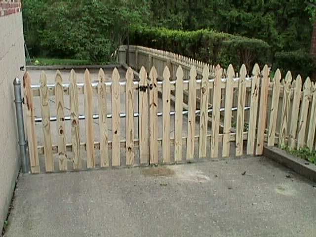 A wooden picket fence is sitting on the side of a road.
