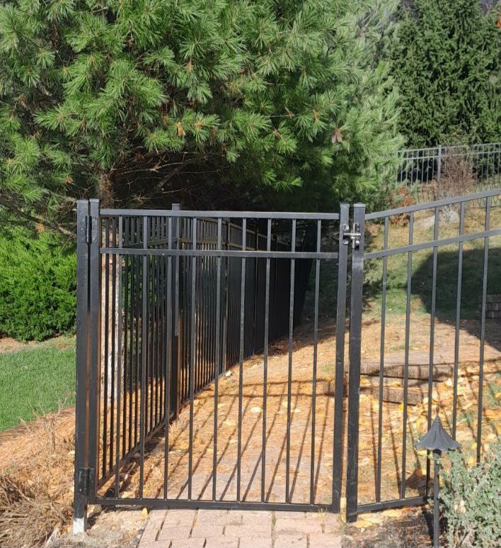 A black wrought iron gate leading to a brick walkway surrounded by trees.