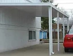 White carport attached to a white building; a red car is parked under it.