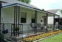 White house with black porch railings, awning, and flower bed.