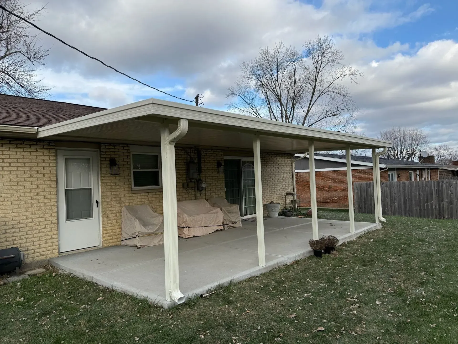 Concrete patio with cream-colored awning and support posts attached to a brick home.