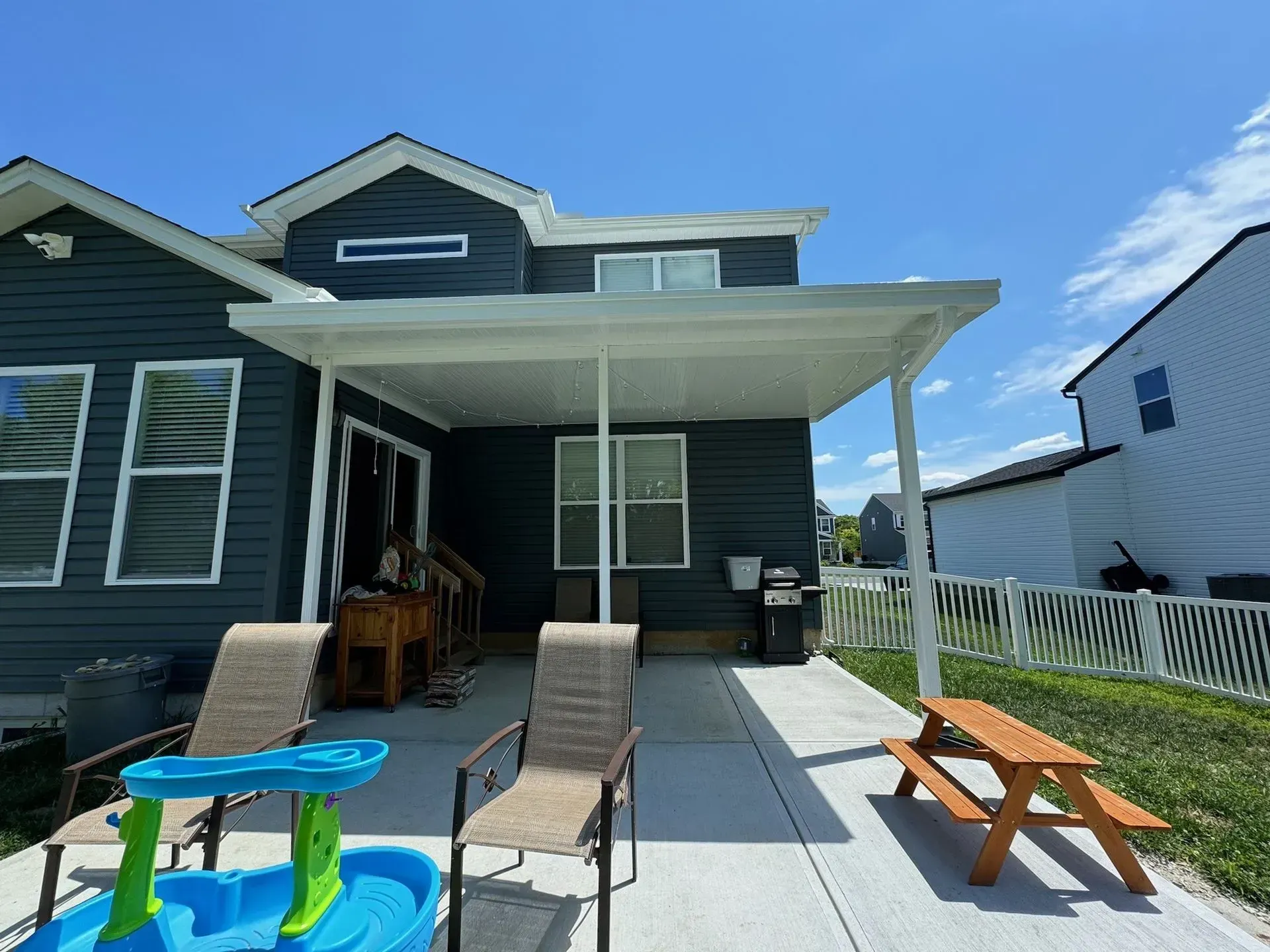 Patio with a blue house, white awning, and outdoor furniture on a sunny day.