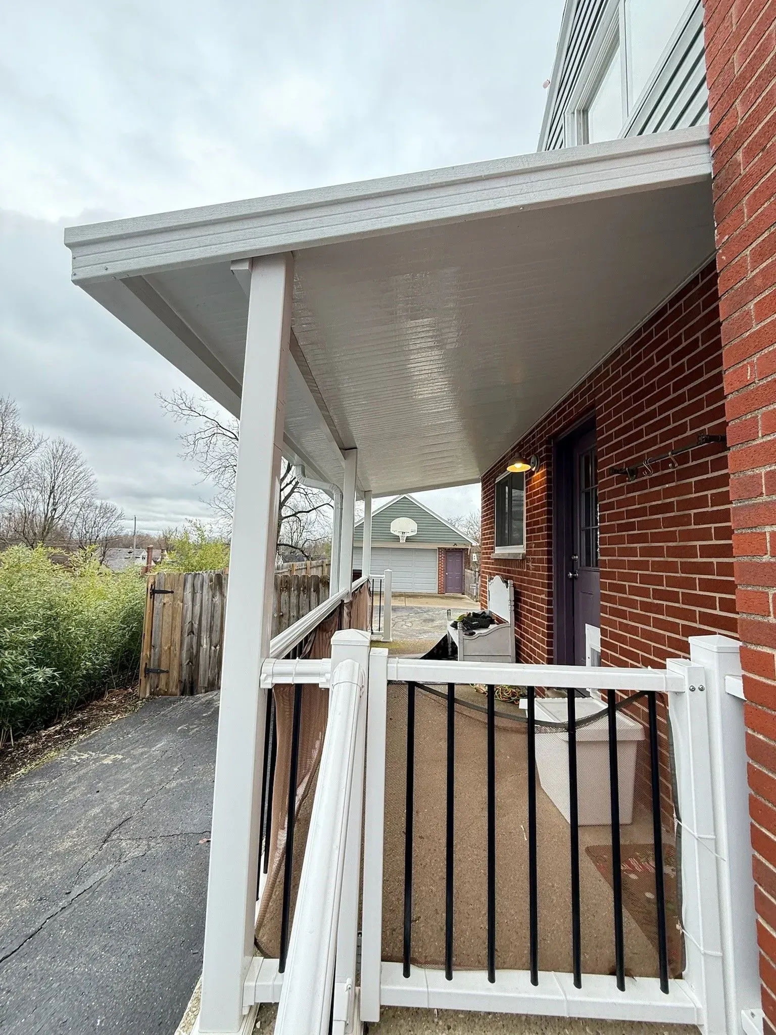 Covered porch with white posts, railing, and roof attached to a brick building.