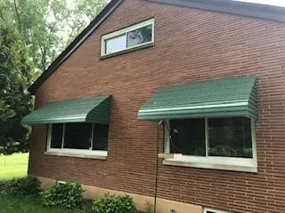 Red brick house with green awnings over two windows. Another window is above.