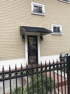 Tan building with black door, awning, two windows, and black fence.