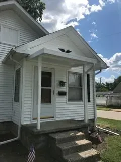White house with porch and steps, blue sky visible.