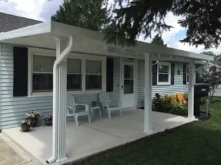 White-roofed porch covers a light blue house. White chairs sit on the concrete porch. Black shutters frame windows.