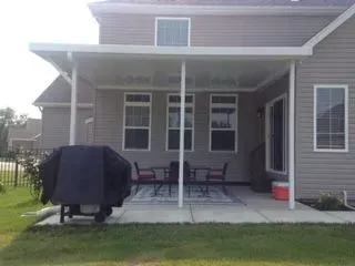 Patio cover attached to a house with outdoor furniture, grill, and rug.