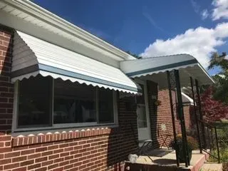 Brick house exterior with white and blue awnings over the window and doorway.