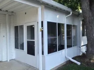 White-walled sunroom with glass windows and a screened door; a tree trunk is on the right.