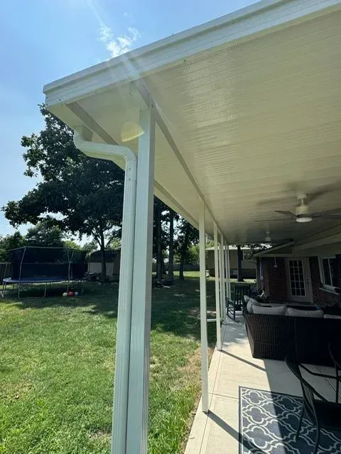 White covered patio with gutter, posts, and ceiling fan, overlooking a backyard.