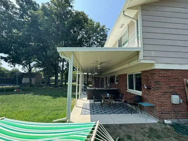 A covered patio with outdoor furniture, next to a red brick house, with a hammock in the foreground.