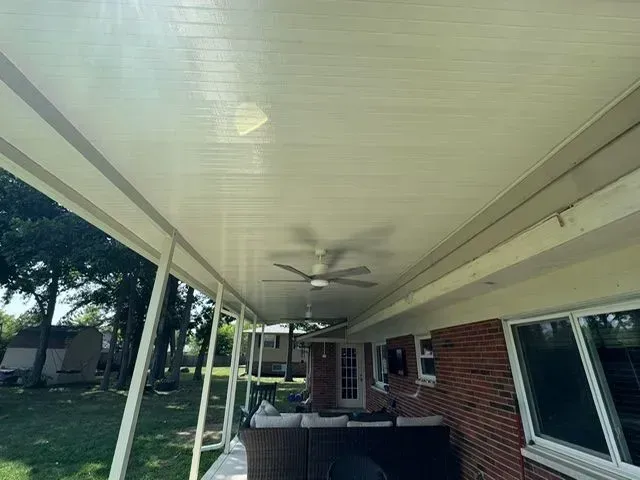Covered outdoor patio with a ceiling fan, beige ceiling, and view of a yard.
