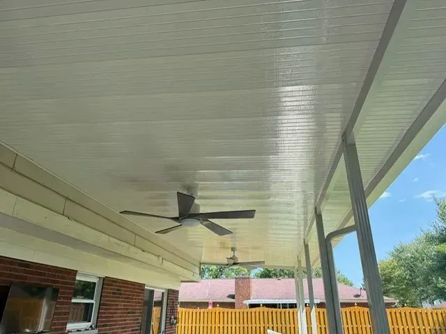 White outdoor ceiling with ceiling fans, attached to a porch with brick and fence in the background.