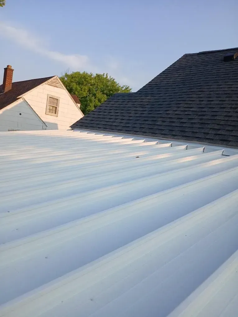 White corrugated metal roof with adjacent house, blue sky.