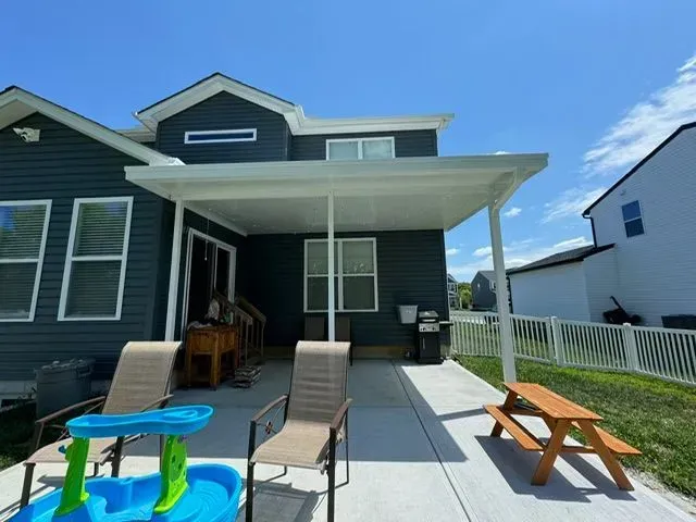 Patio with a white covered roof, chairs, a small table, and a house with blue siding.