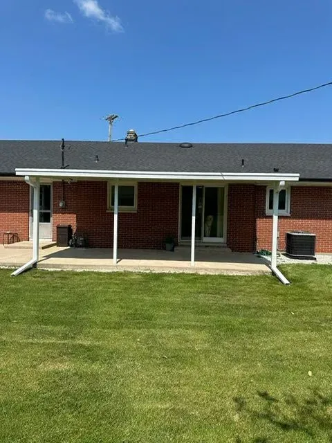 Backyard view of a brick house with a white-framed covered patio and green lawn under a blue sky.