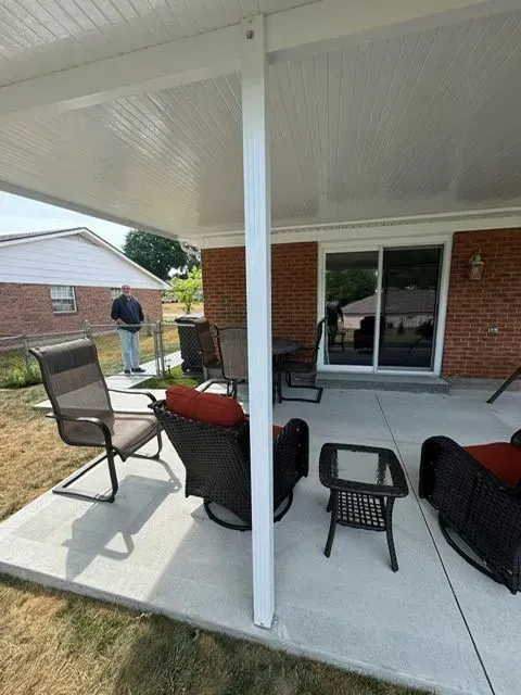 Covered patio with seating, brick wall, and person standing in yard.
