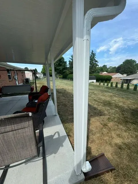 White patio roof with matching gutter and downspout, concrete patio, lawn, and blue sky.