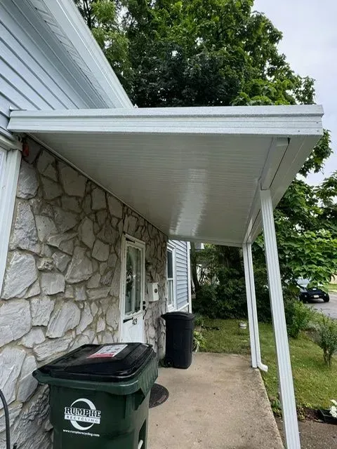 White covered porch attached to a house with stone siding. Trash cans are visible in front of the door.