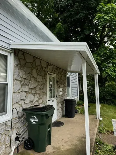 White awning over a stone-walled porch with a green trash bin.