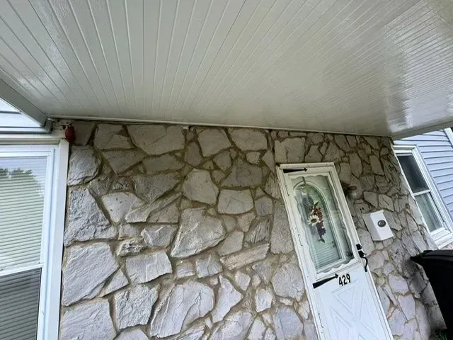 White-paneled ceiling over stone wall facade with a white door and windows.