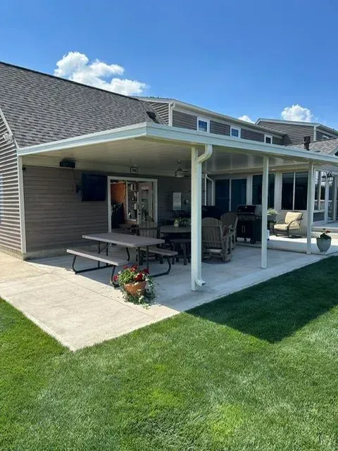 Patio with a covered seating area, picnic table, grill, and outdoor furniture. Green lawn and sunny day.