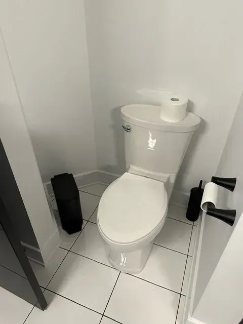 White toilet in a small bathroom with black accents. Toilet paper and brush are visible.