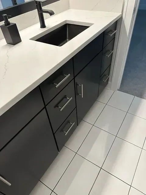Bathroom vanity with black cabinets, white countertop, and white tile floor.