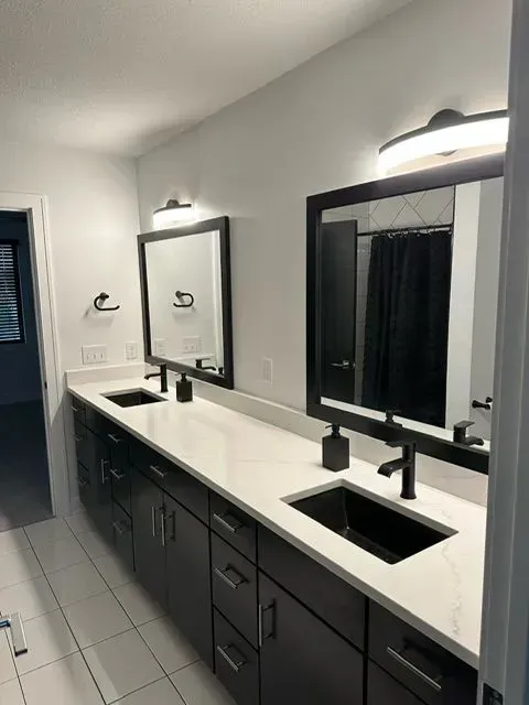 Modern bathroom with double vanity, black fixtures, white countertop, and large mirrors.