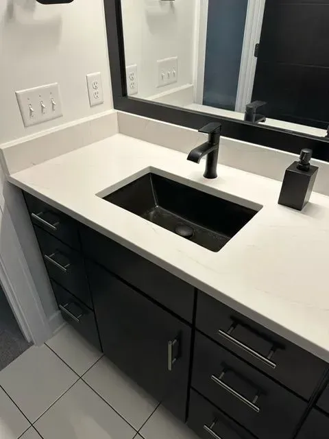 Bathroom vanity with black sink, faucet, and dark brown cabinets with white countertop and mirror.