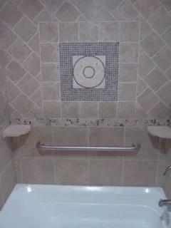 Bathroom with beige tile, a decorative square mosaic, a grab bar, and a bathtub.