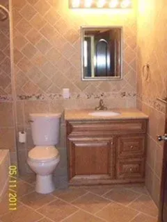 Bathroom with a toilet, vanity, mirror, and tiled walls and floor.