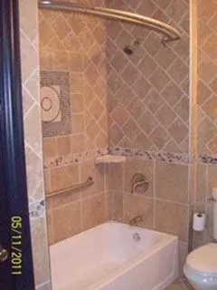 Bathroom with beige tile, white tub, curved shower rod, and grab bar.