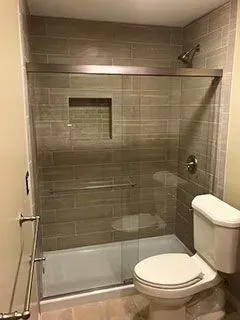 Bathroom with tan tile, glass shower, toilet.