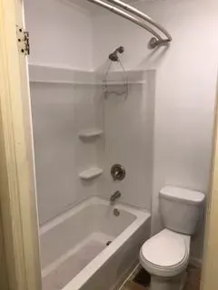 White bathroom with a tub, showerhead, and toilet.