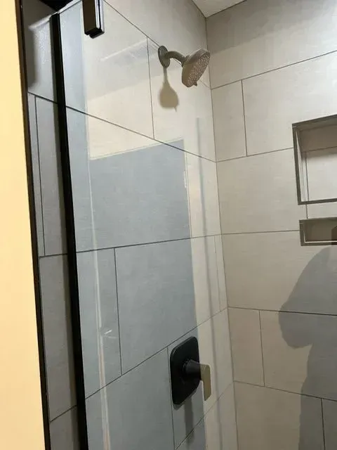 Shower stall with glass door, white tiled walls, and black fixtures.