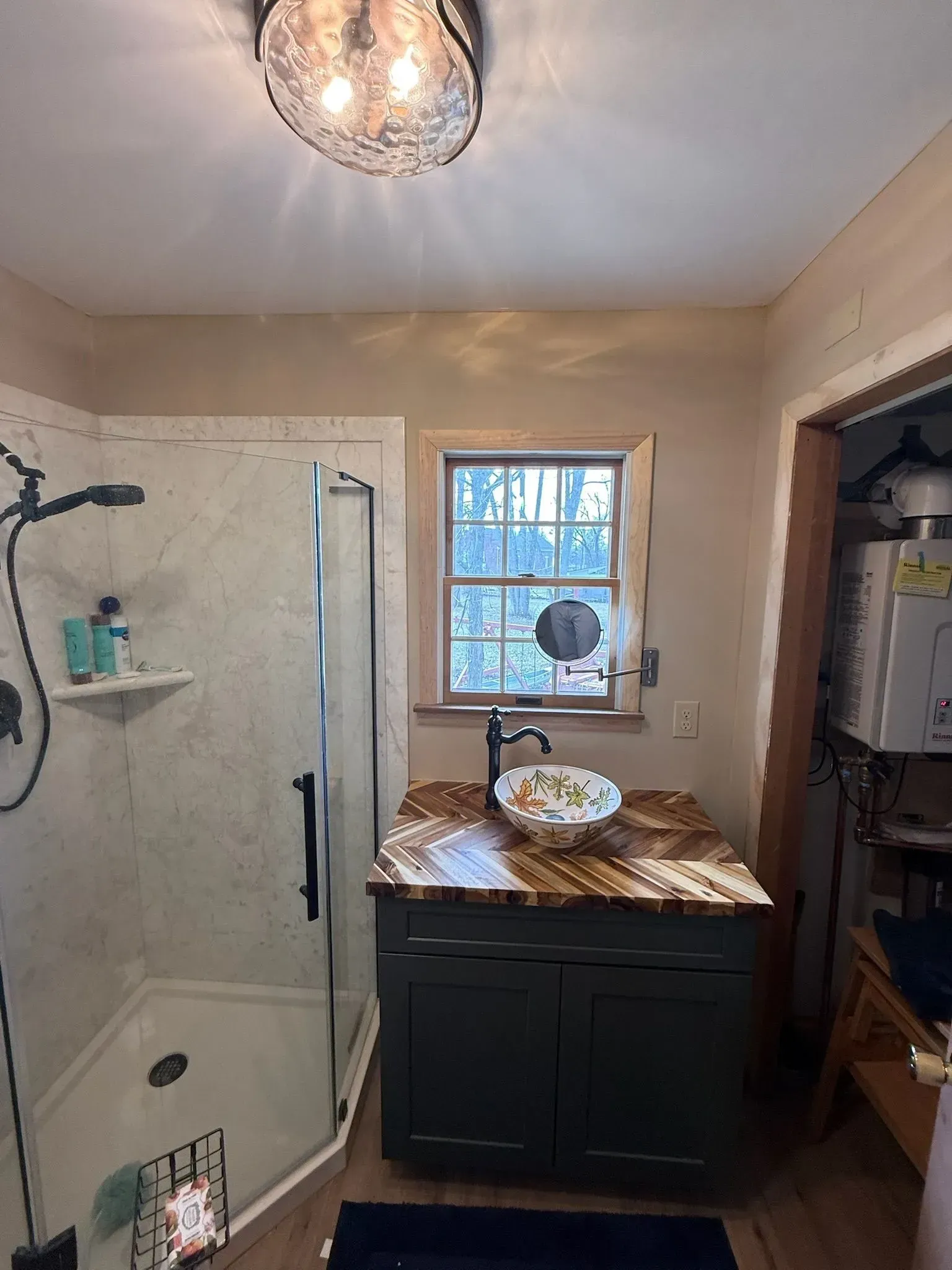 Bathroom with shower, vanity, and window. Teal vanity cabinet, marbled shower, and patterned countertop.