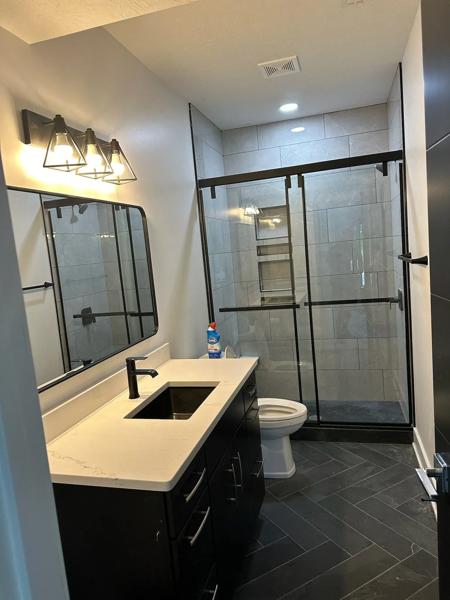 Modern bathroom with black vanity, gray tiled shower, and dark floor.
