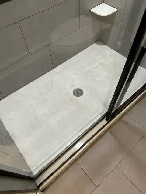 Shower stall with light-colored floor and drain, glass doors, and tiled walls.