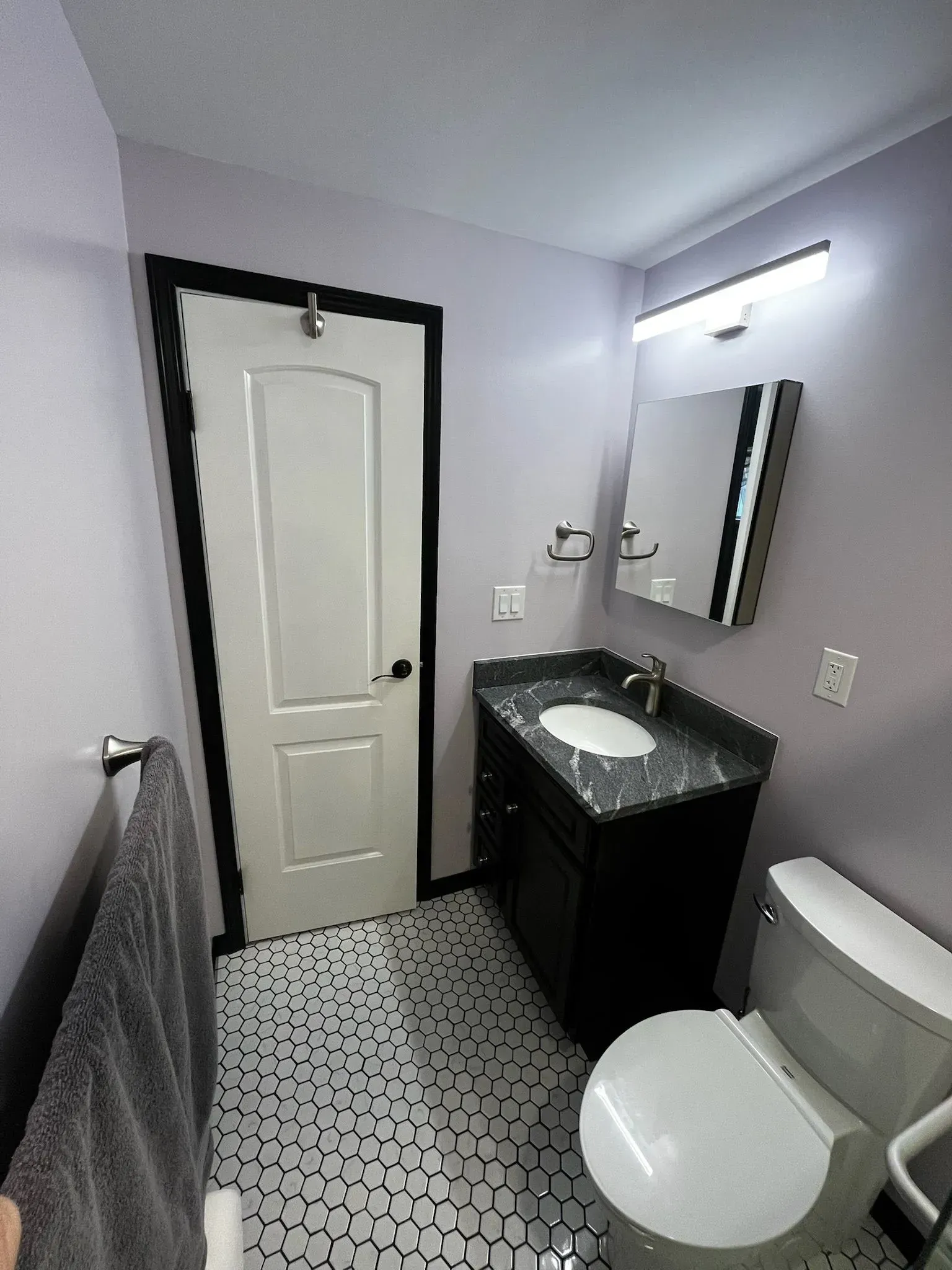 Bathroom with lavender walls, black-framed door, vanity, toilet, and patterned floor.