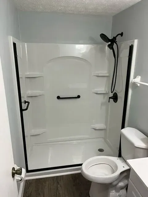 Bathroom with a white shower, black fixtures, toilet, and light blue walls.