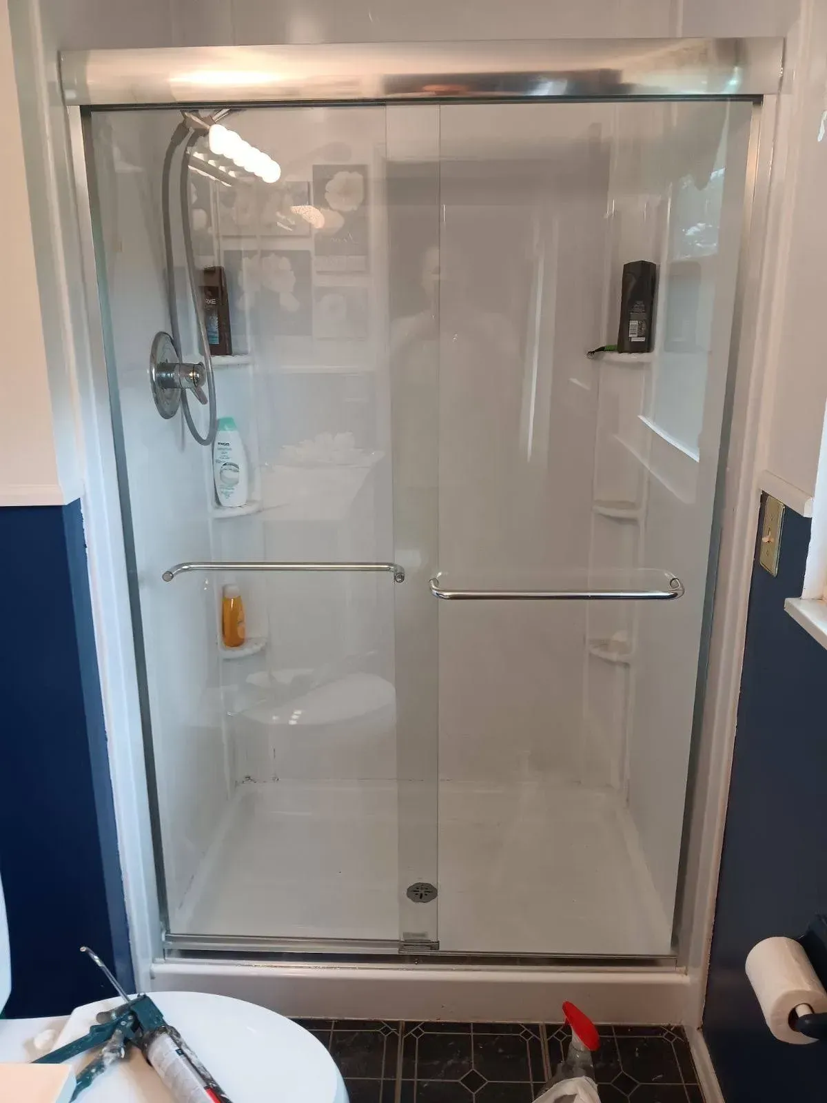 Shower stall with sliding glass doors, chrome fixtures, white walls, and a small built-in shelf.