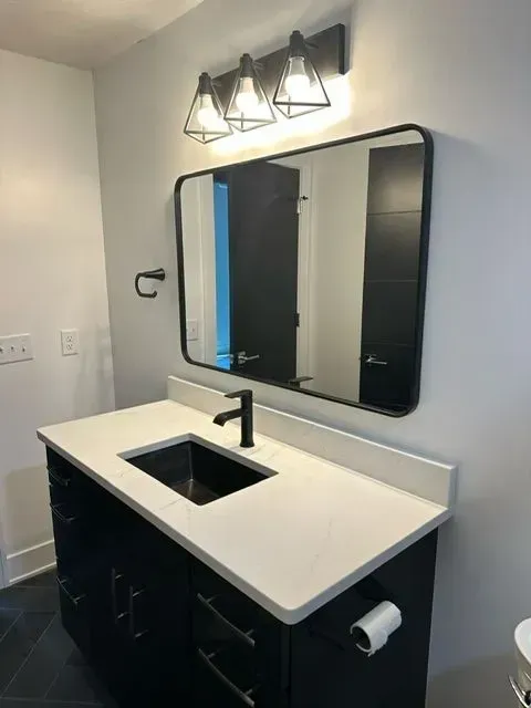 Modern bathroom with black vanity, white countertop, rectangular mirror, and black faucet.