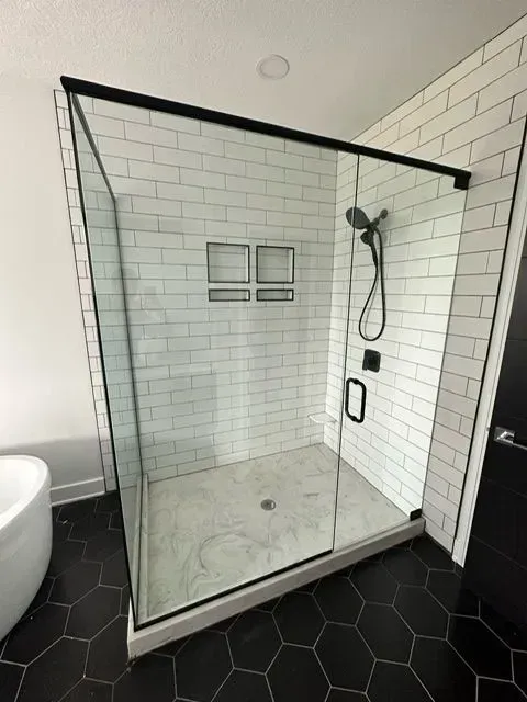 Modern shower with black trim, glass doors, subway tile walls, and a black hexagon tile floor.