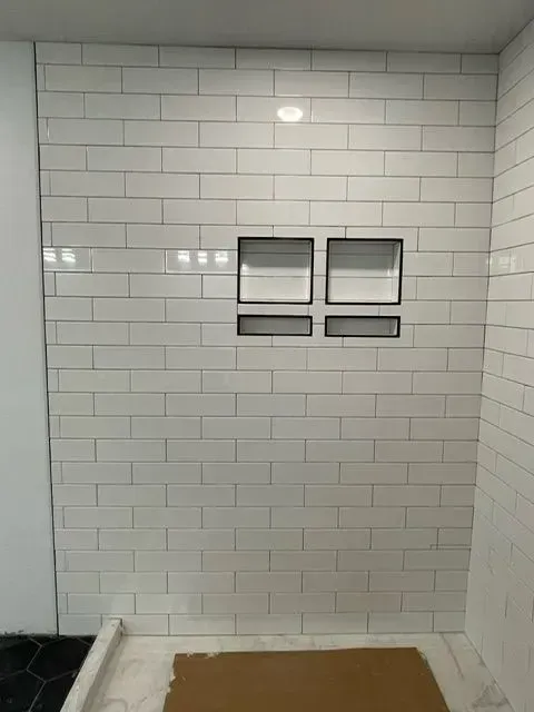White tiled shower wall with recessed shelves, and white grout.