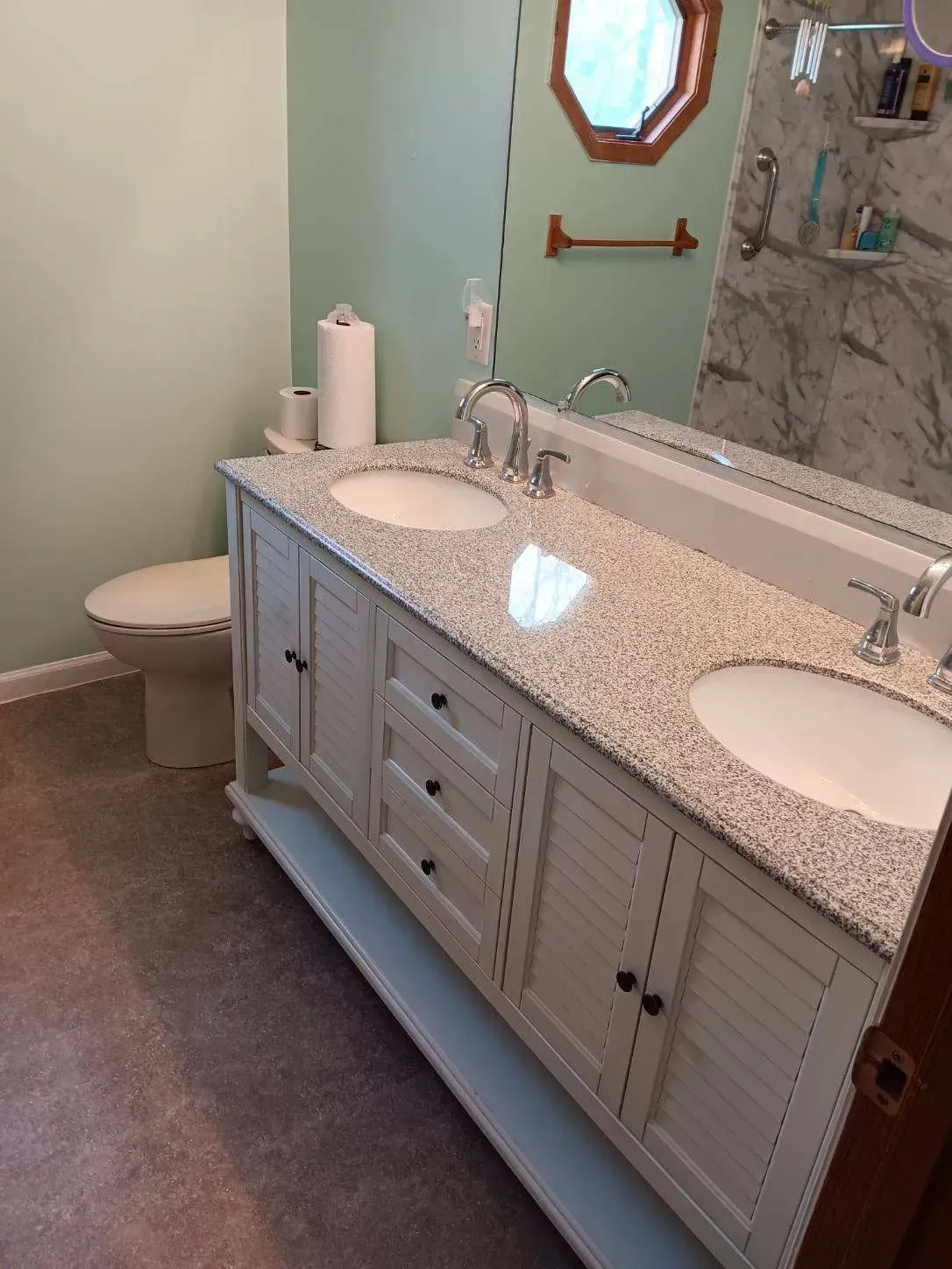Bathroom with a white double-sink vanity, marble shower wall, and light green walls.