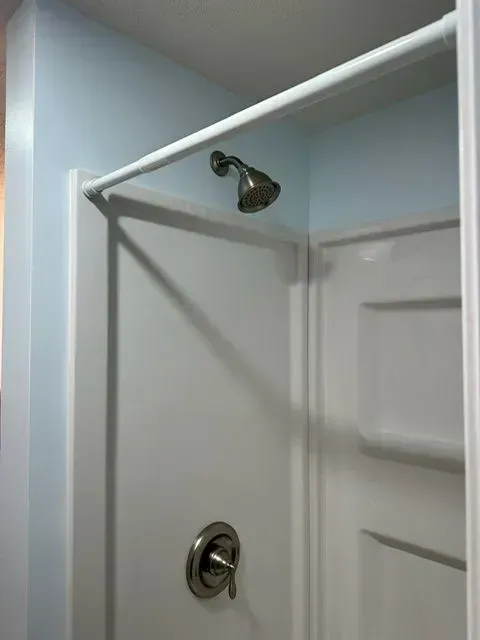 White shower stall with a silver showerhead and faucet against a light blue wall.