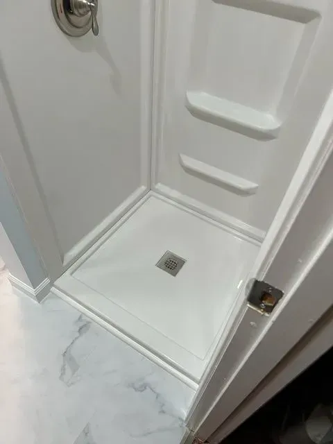 White shower stall with shelves, drain, and open door on a tile floor.