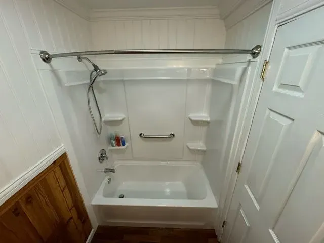 Small white bathroom with a tub and shower combination; includes a grab bar.